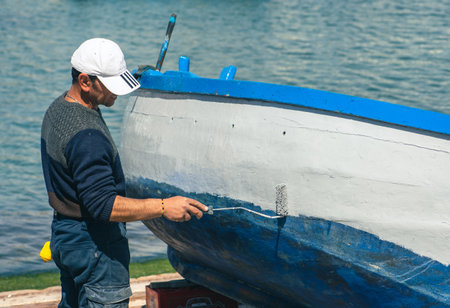 Bari, Puglia, Italy - April 8 2023: Fisherman repairing and painting an old wooden fishing boat at the port quay in Bari, Puglia Italyのeditorial素材