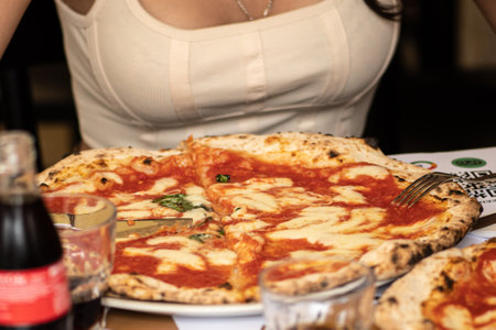Girl eating hot pizza Margherita with tomato sauce, mozzarella and basil in a pizzeria or restaurant in Italyの写真素材
