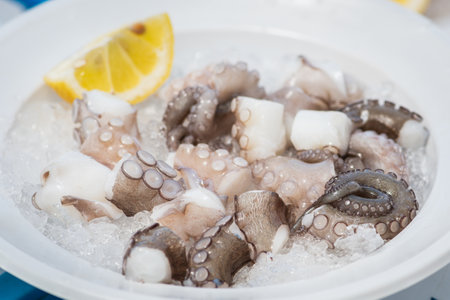 Plate of raw fresh pieces of octopus with lemon and ice ready to eat in a fish market in Bari, Puglia, Italyの写真素材