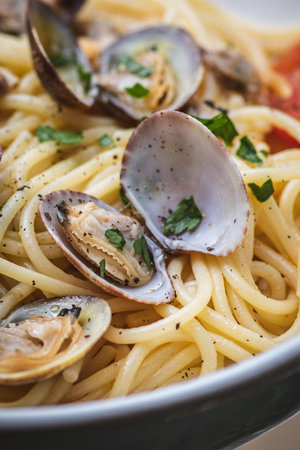 Spaghetti with clams, fresh cherry tomatoes, parsley leaves and ground black pepper, close up, verticalの写真素材
