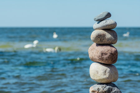 Balancing stones on a big rock with sea grass on the beach, with blue water waves on background, Baltic Sea, Olando Kepure, Lithuaniaの写真素材
