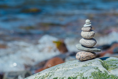 Balancing stones on a big rock with sea grass on the beach, with blue water waves on background, Baltic Sea, Olando Kepure, Lithuaniaの写真素材