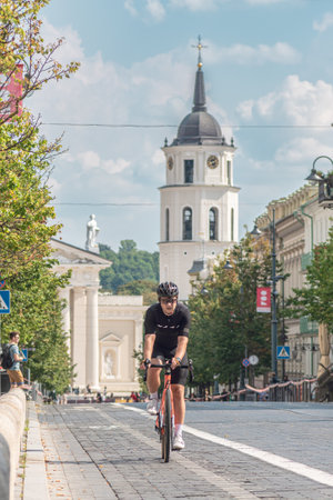 Vilnius, Lithuania - August 20 2023: Boy riding a road bike with helmet on the bike road in the city center of Vilnius, Lithuania with tower bell and cathedral on background, vertのeditorial素材