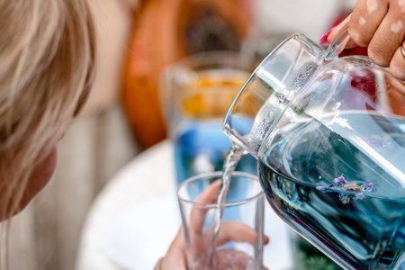 Blonde hair child holding a glass cup while is filled with butterfly pea or blue pea tea, herbal tea infusion, close upの写真素材
