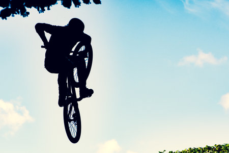 Silhouette of a biker performing an extreme dirty jump with a bmx bike against the skyの写真素材
