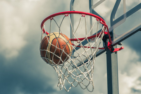 Basketball orange ball is entering the hoop or basket. Playing in the street on outdoor court with a...