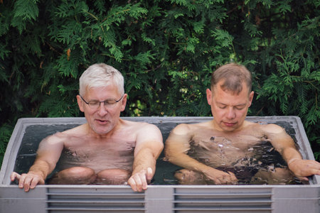 Couple of male friends ice bathing in the cold water among ice cubes. Wim Hof Method, cold therapy, breathing techniques, yoga and meditationのeditorial素材