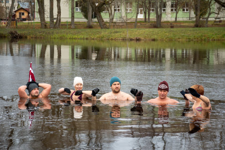 Preili, Latvia - November 18 2023: Girl ice bathing with gloves and hat in the cold water of a lake in Preili, Latvia. Wim Hof Method, cold therapy, breathing techniques, yoga andのeditorial素材