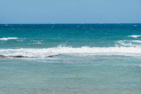 Scenic view of ocean waves crashing onto the shore under a clear blue sky. A tranquil seascape...