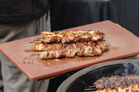Juicy skewered meat grilled on a board and ready to eat during barbecue with smoke rising