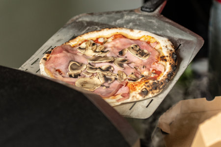 Lifting a freshly baked pizza from an electric oven using a pizza peelの写真素材