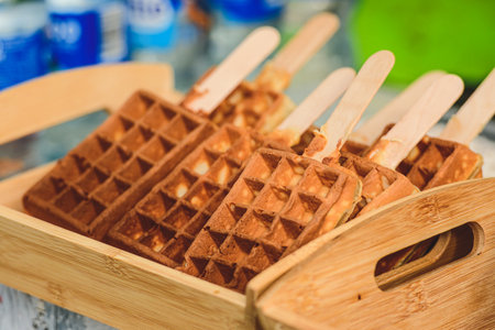 Crispy golden waffles served on wooden sticks, arranged neatly in a bamboo tray. A creative and...