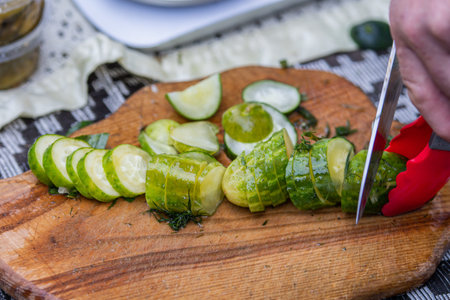 Close-up of pickled cucumbers being sliced on a wooden cutting board. Traditional homemade snack from fermented vegetables, popular in Eastern European cuisineの写真素材
