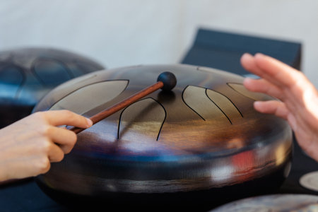 Hands playing a steel tongue drum with a mallet. Close-up of a melodic percussion instrument used in meditation, yoga, sound therapy, and relaxation musicの写真素材