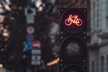 Close-up of red bicycle traffic light signal illuminated against urban street background at dusk,...