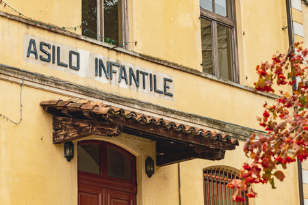 Historic building facade in Monteu da Po, Italy, with a weathered sign. The yellow plaster walls, wooden door, and autumn leaves create a nostalgic and charming scene.の写真素材