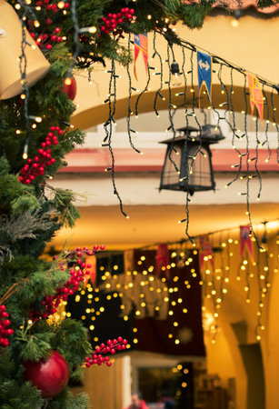 Festive Christmas decorations with glowing string lights, evergreen branches, red berries, and hanging ornaments creating a warm and cheerful holiday atmosphereの写真素材