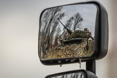 Ukraine - November 22 2025: Reflection of a camouflaged armored military vehicle with a mounted cannon pointing towards the sky seen in a side mirror, captured outdoors on an overcのeditorial素材