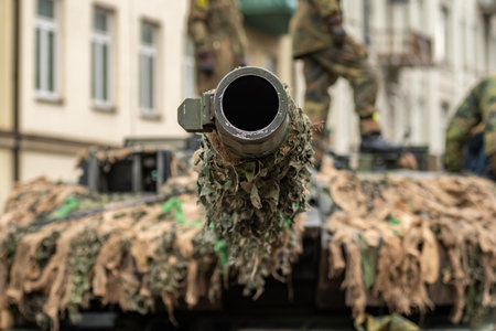 Ukraine - November 22 2025: Ukraine - November 22 2025: Close-up of a camouflaged tank cannon pointing towards the sky in an urban setting, with building with soldiers walking on tのeditorial素材