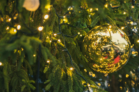 Close-up detail of a Christmas tree with a shiny golden bauble, surrounded by twinkling lights and green pine needlesのeditorial素材