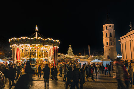 Vilnius, Lithuania - November 30 2025: Beautiful carousel at night in a festive city square in Vilnius, Lithuania, Europe, surrounded by people, holiday lights and market stallsのeditorial素材