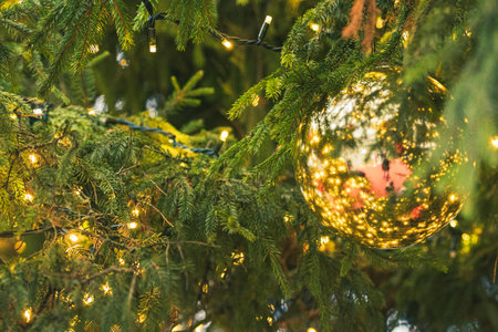 Close-up detail of a Christmas tree with a shiny golden bauble, surrounded by twinkling lights and...