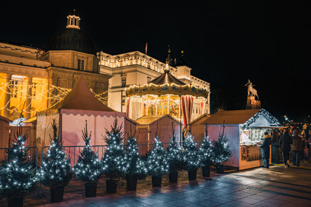 Vilnius, Lithuania - November 30 2025: Carousel and Christmas trees at night in a festive city square in Vilnius, Lithuania, Europe, surrounded by people, holiday lights and marketのeditorial素材