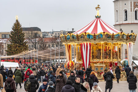 Vilnius, Lithuania - November 30 2025: A brightly lit Christmas tree with carousel in a festive city square in Vilnius, Lithuania, Europe, surrounded by people, holiday lights andのeditorial素材