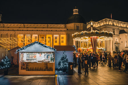 Vilnius, Lithuania - November 30 2025: Beautiful carousel at night in a festive city square in Vilnius, Lithuania, Europe, surrounded by people, holiday lights and market stallsのeditorial素材