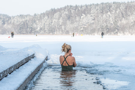 Vilnius, Lithuania - January 11 2026: Beautiful blonde hair woman immersed in the freezing cold water of a lake practicing cold water swimming. Wim Hof Method, cold therapy, breathのeditorial素材