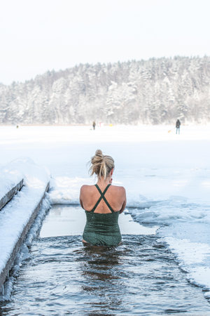 Vilnius, Lithuania - January 11 2026: Beautiful blonde hair woman immersed in the freezing cold water of a lake practicing cold water swimming. Wim Hof Method, cold therapy, breathのeditorial素材