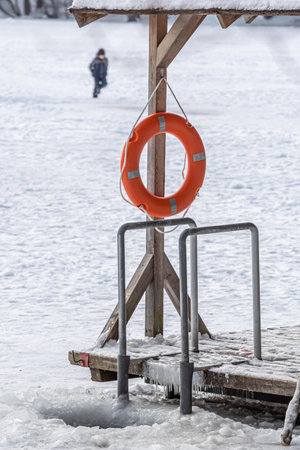 Hole in a frozen lake with wooden pier and lifesaver covered in snow ready for cold therapy, ice bathing. Cold therapy, breathing techniques, yoga and meditationの写真素材