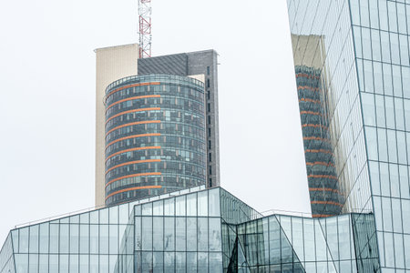 Modern glass office buildings with reflective windows and geometric architecture against a cloudy sky in Vilnius, symbolizing corporate growth, urban developmentの写真素材