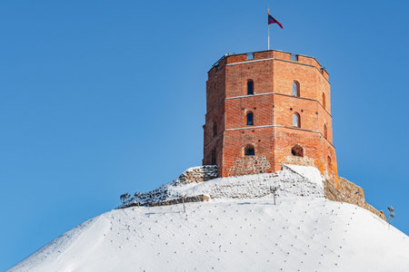 Gediminas Tower or Castle, the remaining part of the Upper Medieval Castle on the hill covered by the snow, Vilnius, Lithuania with Lithuanian flag in a winter sunny dayの写真素材