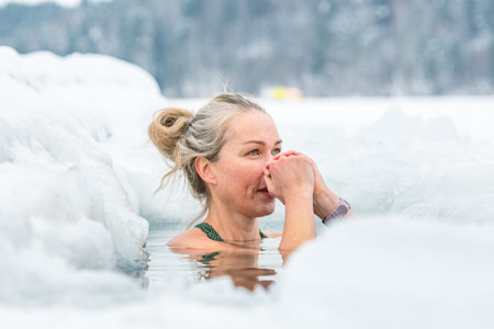 Vilnius, Lithuania - February 8 2026: Beautiful blonde hair woman immersed in the freezing cold water of a lake practicing cold water swimming. Wim Hof Method, cold therapy, breathのeditorial素材