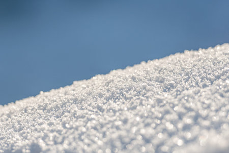 A close-up view of sparkling snow crystals, softly illuminated by sunlight, creating a bright, textured winter background with a serene and minimalist feelの写真素材