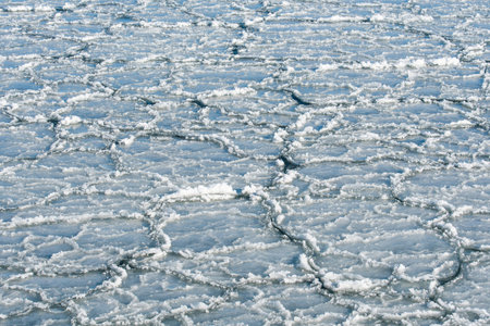 Floating sea ice and scattered ice floes forming abstract patterns on cold dark water, creating a...