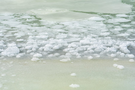 Floating sea ice and scattered ice floes forming abstract patterns on cold dark water, creating a...