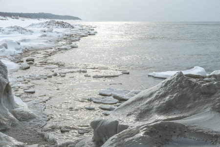 Icy winter seascape with frozen waves, floating ice floes on the sea water along a snowy shoreline...