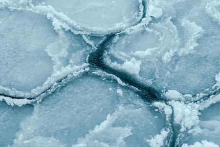 Floating sea ice and scattered ice floes forming abstract patterns on cold dark water, creating a...