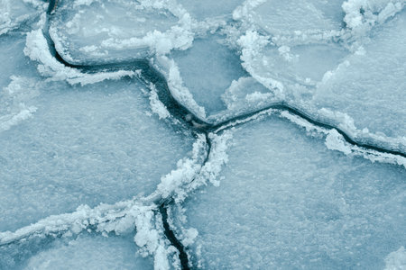 Floating sea ice and scattered ice floes forming abstract patterns on cold dark water, creating a...
