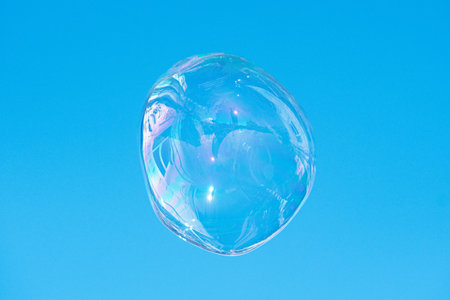 Floating soap bubble reflecting a city and the architecture against a clear blue sky, creating a...