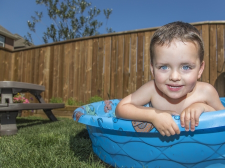 close up of a young boy looking out of a paddling pool with picnic table in the back groundの写真素材