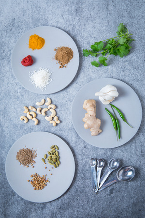 Ingredients for curry paste on round plates and a grey background. Seeds, spices, coriander, garlic, chillies, ginger, cashews for Indian curry paste ingredients.の写真素材