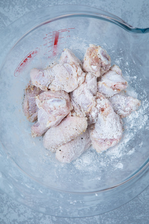 Pieces of floured and enwrapped chicken wings in a glass contained. Grey background.の写真素材