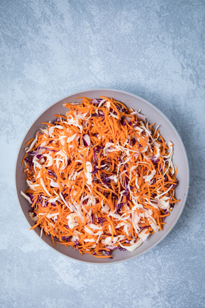 Top view of grated carrots and cabbage in a deep white bowln. Grey background.の写真素材