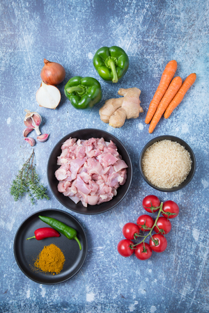Top view of raw chicken and rice in dark bowls with root vegetables on the kitchen counter. Indredients for African jollof rice. Ingredients for exotic rice.の写真素材