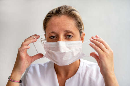 Young female caregiver putting on surgical mask