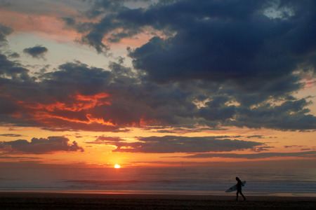 Surfer on the ocean beach at sunset with dark cloudsの写真素材