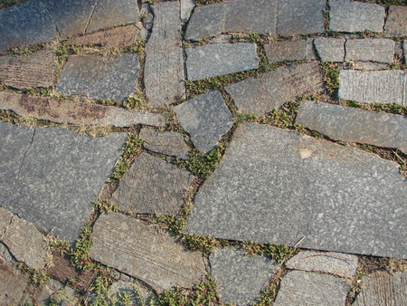 texture, background. The pavement of granite stone. Paved roadway street. any paved area or surface. Old cobblestone road pavement texture, grass between stonesの写真素材